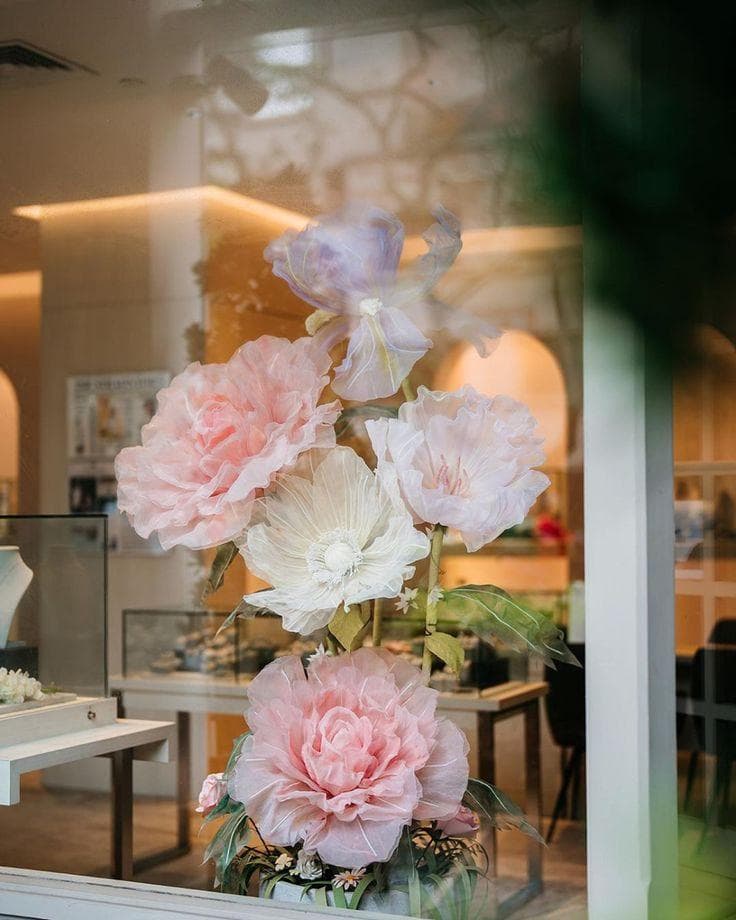 Pivoines géantes rose pâle et crème en organza, vues à travers la vitrine d'une bijouterie