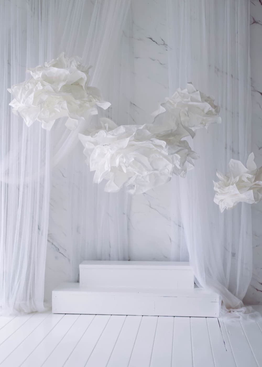 Grandes fleurs blanches en soie suspendues devant un voilage et un mur de marbre