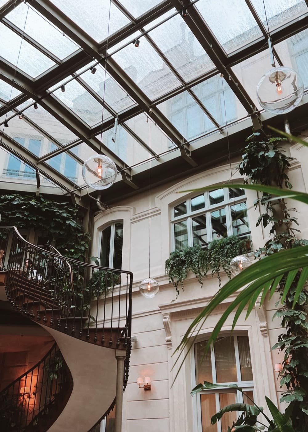 Patio couvert d'une verrière, façades crème tapissées de lierre et de plantes retombantes
